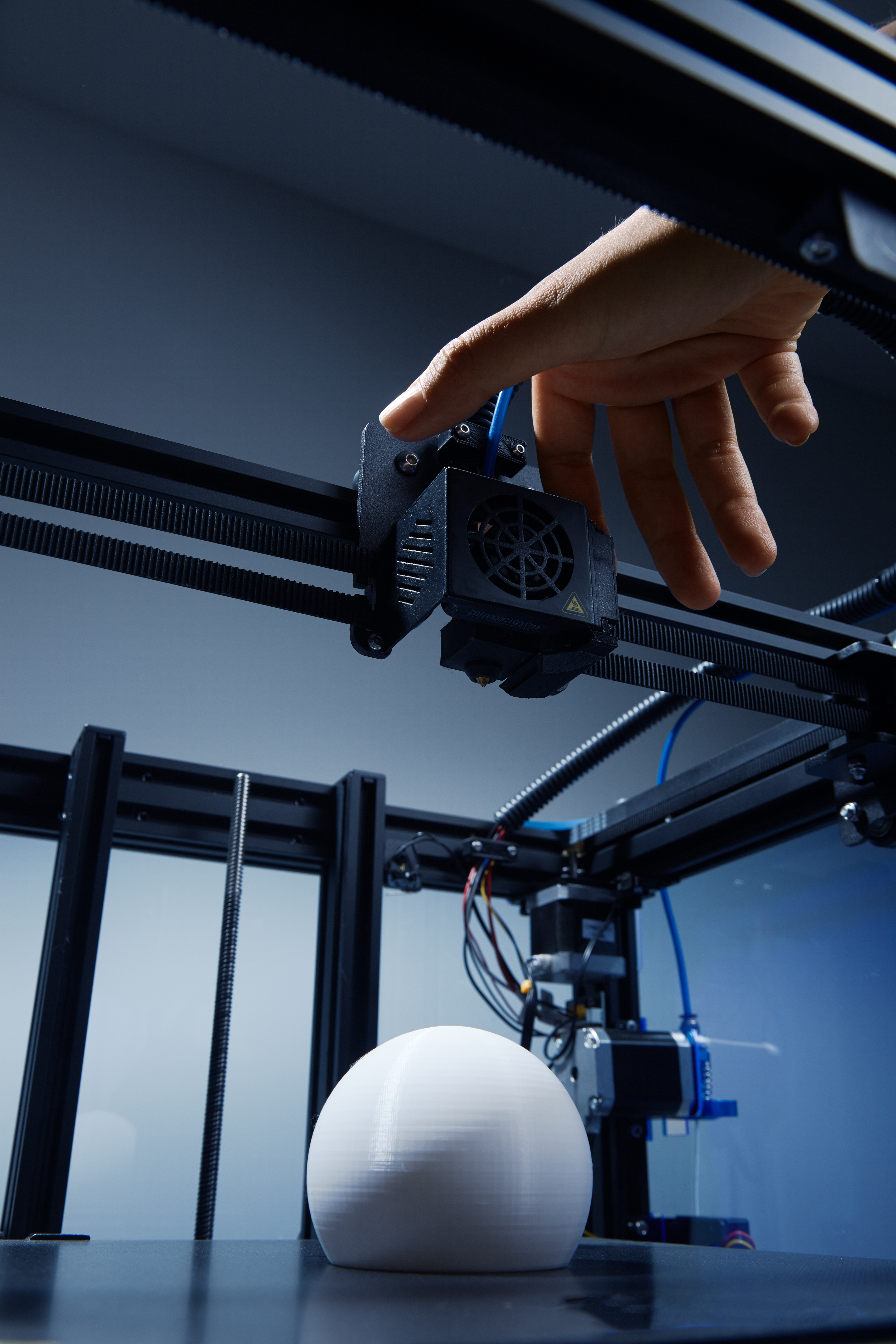 A gender-neutral hand modifying settings in 3d printer, to finish printing round white object from recycled plastic. Futuristic concept of new working possibilities for small businesses by 3D printing